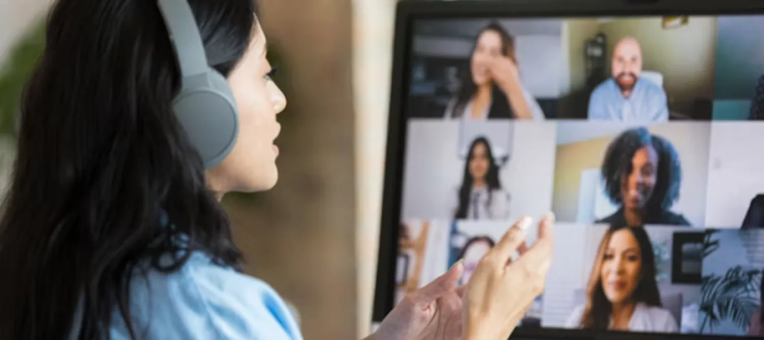 Woman with earphones on facing laptop screen with many faces in an online meeting