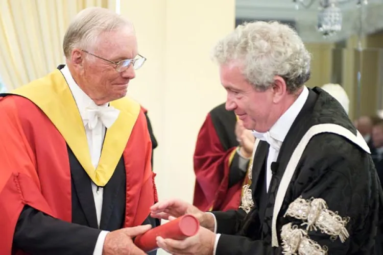 Neil Armstrong in ceremonial robes bring handed a degree in a red tube.