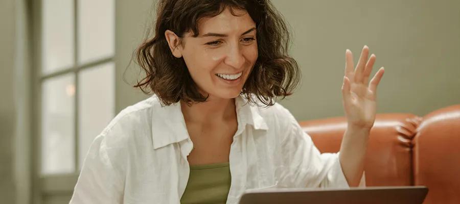 A person speaking and waving to someone on their laptop.