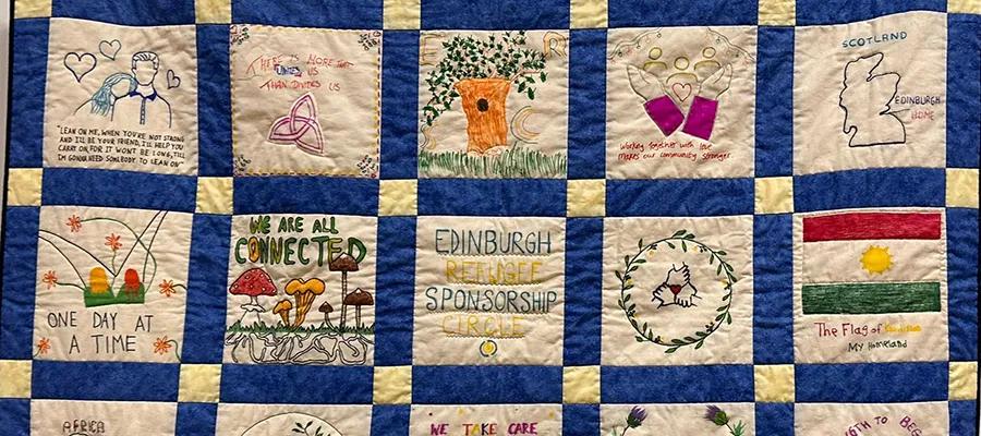A flatlay of a blue and black blanket, with hand-drawn images on each square of the blanket.