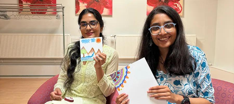Two people smiling and holding up canvases showing their artwork.